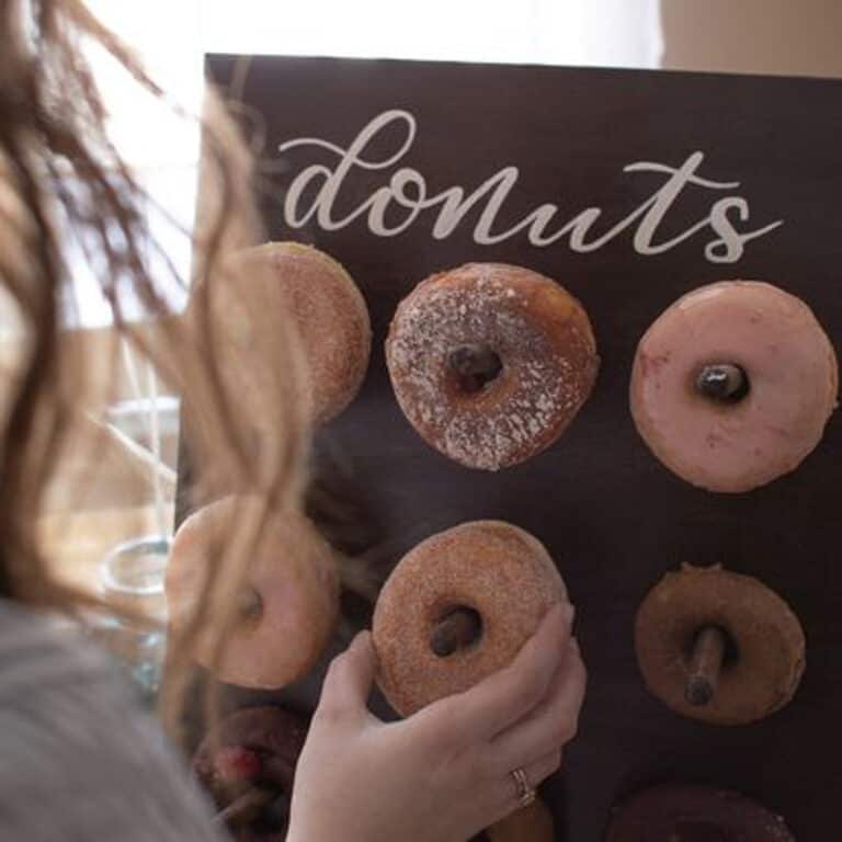 A woman arranges donuts on wooden pegs attached to a blackboard with the word donuts written on it.