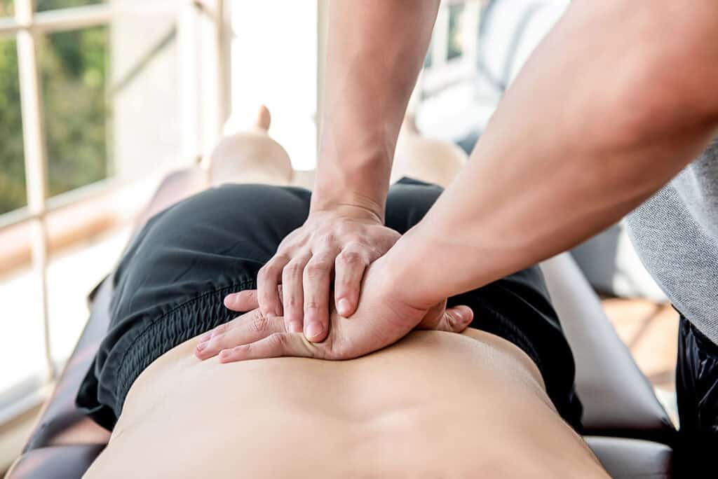 Therapist giving lower back sports massage to athlete male patie